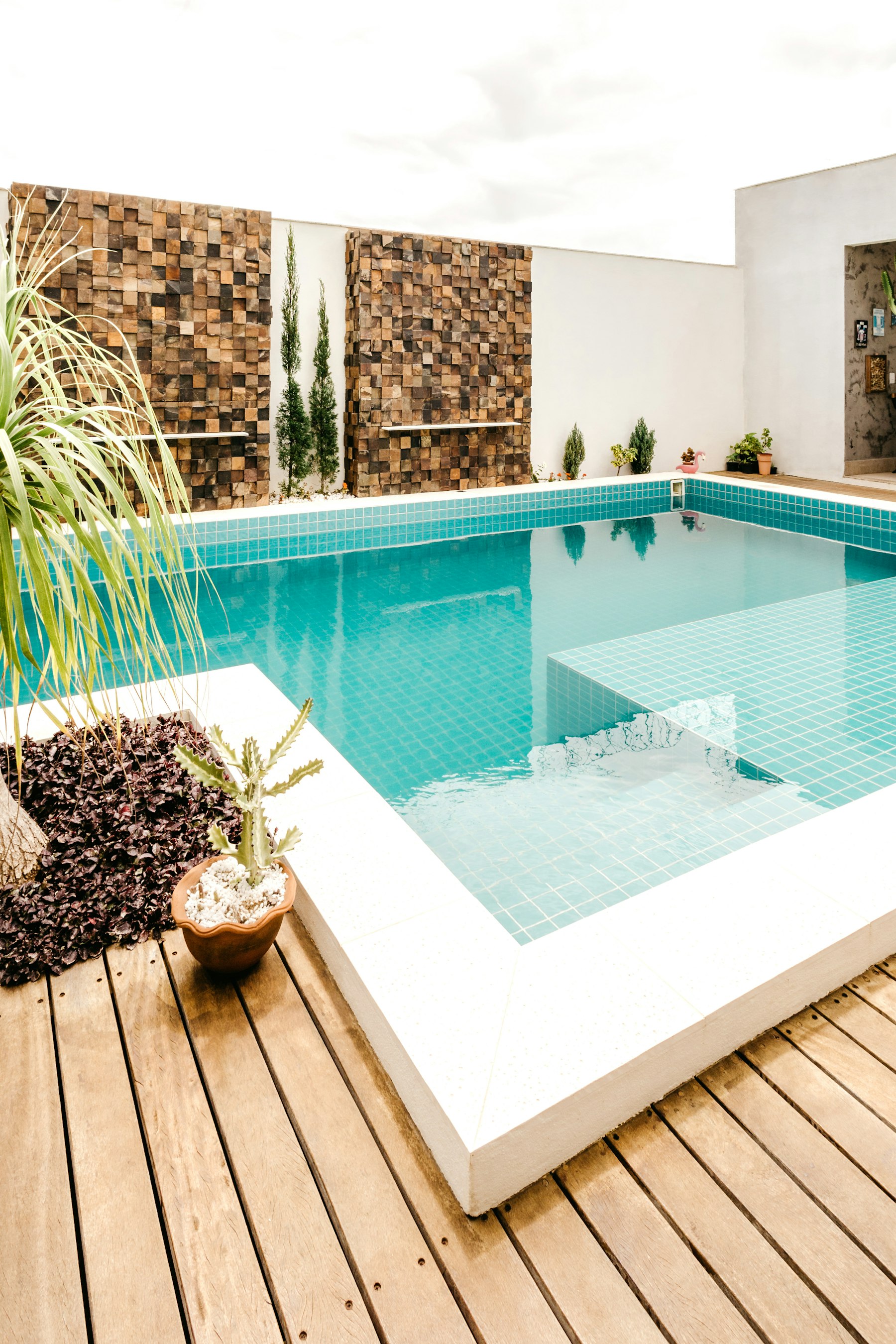 A compact plunge-style pool fully lined in turquoise glass mosaic tile with a submerged bench, potted cactus and agave alongside.